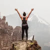 Person standing triumphantly on mountain peak with arms raised.
